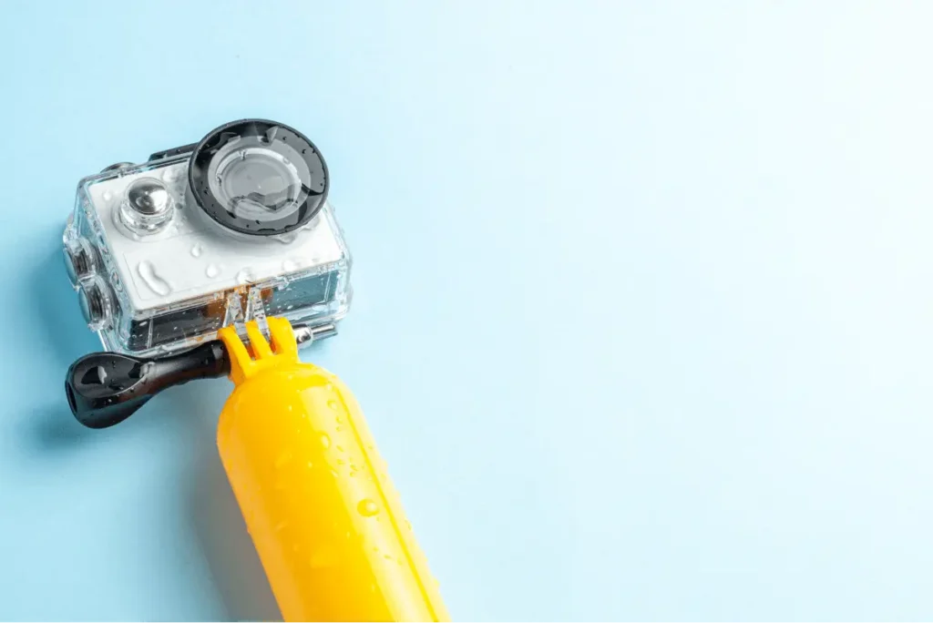 Waterproof action camera on a light blue background, attached to a bright yellow grip for underwater adventures.