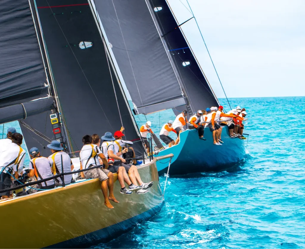 Sailboats racing on turquoise waters, crew members leaning overboard as they maneuver for position.