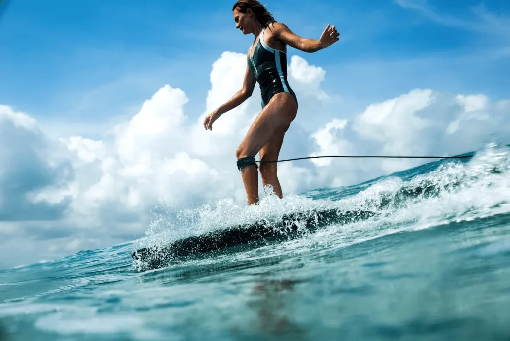 A woman surfing gracefully on a vibrant ocean wave under a bright blue sky with fluffy clouds.