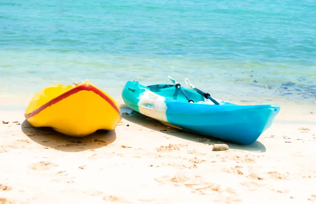 Two colorful kayaks, one yellow and one turquoise, resting on a sandy beach near clear turquoise water.